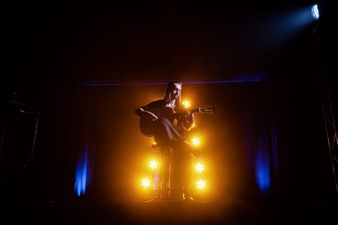 Mastering the First Impression: Your intriguing post title goes here A musician playing an acoustic guitar on stage, illuminated by dramatic yellow and blue lights.