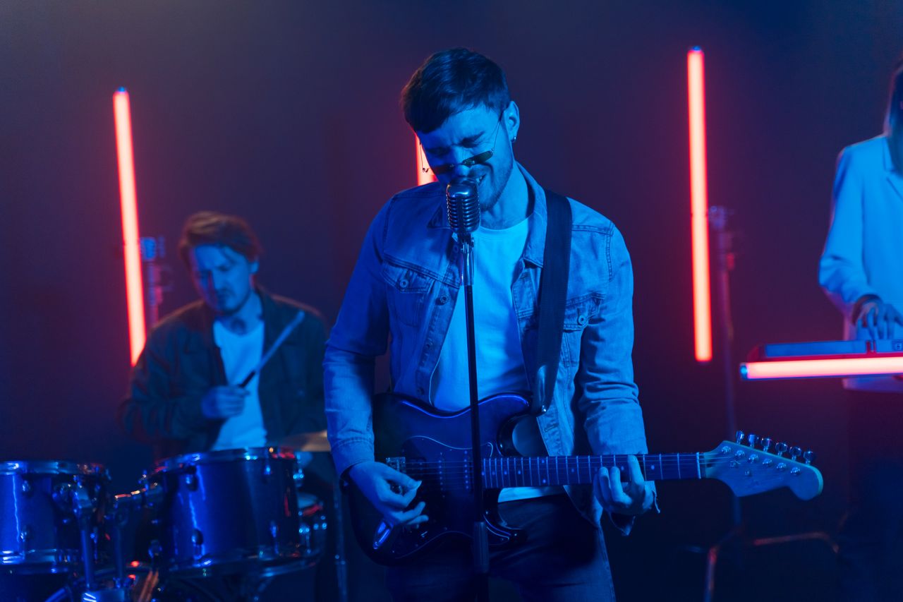 About Vibrant band performing with neon lights, featuring electric guitar and drums.